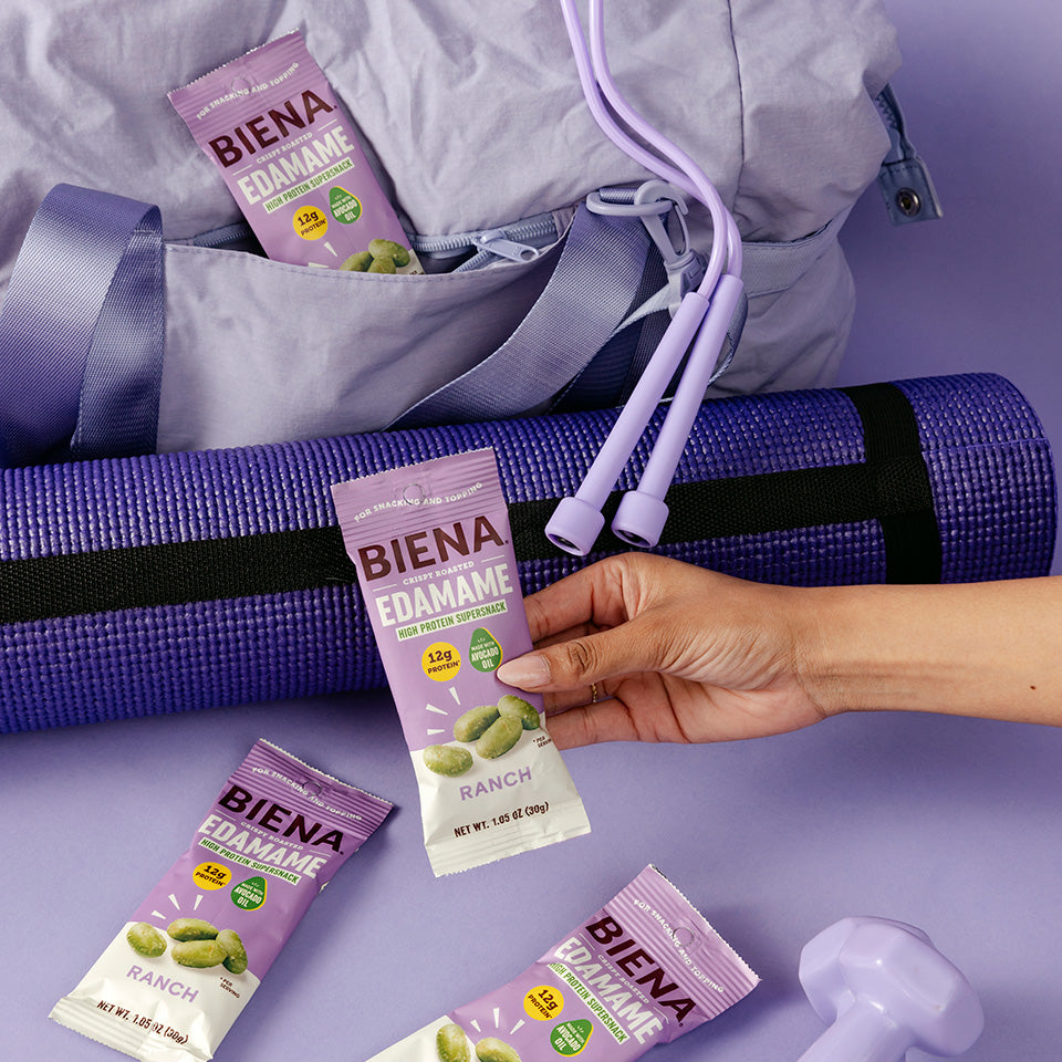 Bag of Biena Crispy Roasted Edamane Ranch Snacks alingside a yoga mat and free weights