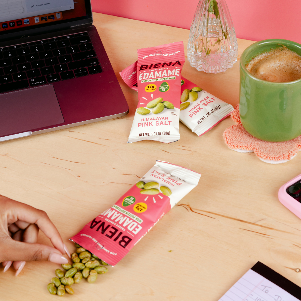 Picture of Biena Crispy Roasted Edamame Himalayan Pink Salt 1oz bags on a desk while someone works at a computer